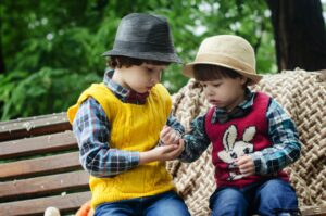 Two young boys in colorful sweaters and hats, sharing and playing outdoors.